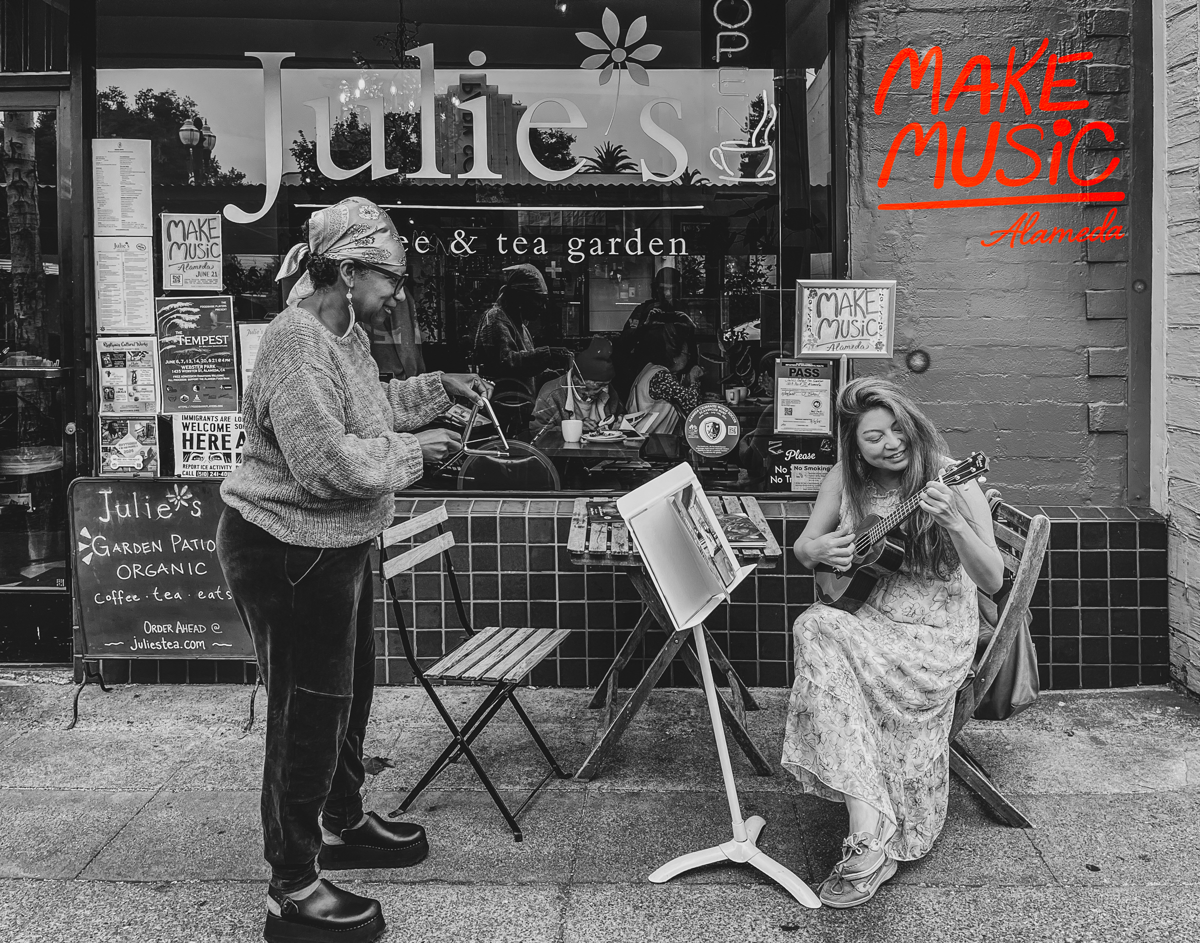 A patron at Julies Coffee and Tea garden plays the triangle with Make Music Alameda 2026 organizer Katherine Park as she sings and plays ukulele on the sidewalk. Photo by Douglas Despres