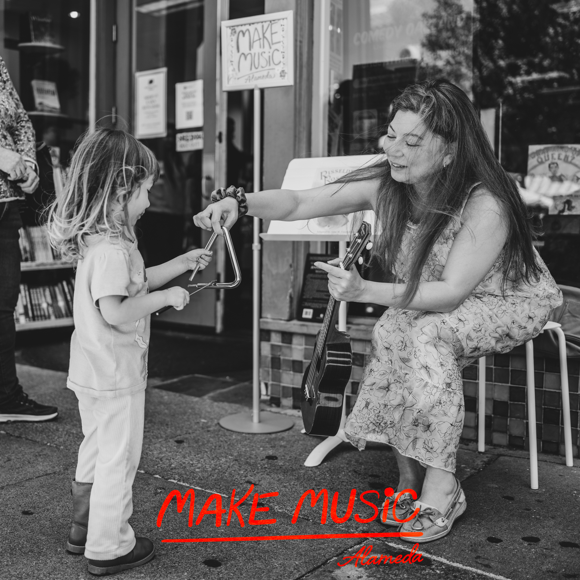 On the sidewalk at Books Inc., Katherine Park holds a ukulele and a triangle while a girl tries playing the instrument. Photo by Douglas Despres
