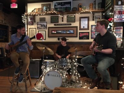 Trio of jazz musicians performing in a pub on bass guitar, drums and guitar